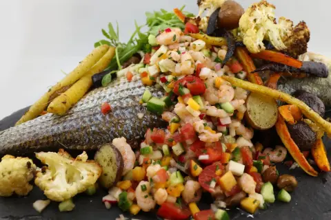 Poisson au barbecue avec salade de crevettes, légumes rôtis et herbes fraîches. Un plat coloré et savoureux.