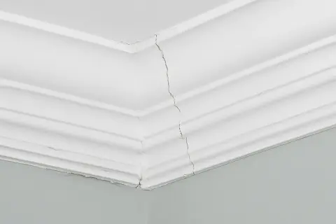 Pęknięta sztukateria w salonie, widoczna na styku ścian i sufitu.