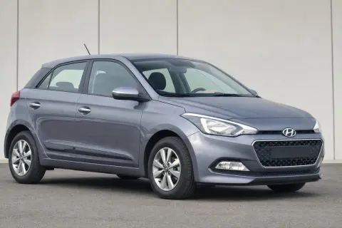 Szary Hyundai i20 z włączonymi światłami pozycyjnymi na tle jasnej ściany.