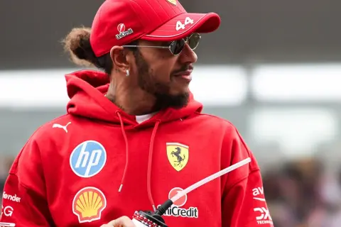 Hamilton, wielokrotny mistrz świata Formuły 1, w czerwonej bluzie z logo Ferrari i okularach przeciwsłonecznych.