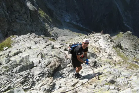 Turysta pokonuje trudny szlak w Rysach, chwytając się łańcuchów.