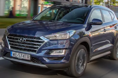 Nowy Hyundai Tucson w ciemnoniebieskim kolorze jedzie ulicą. Elegancki design i nowoczesne linie podkreślają jego dynamiczny charakter.