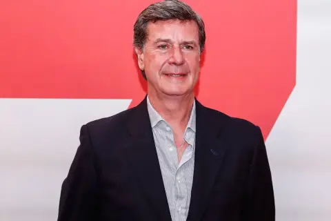 Javier Martínez de Irujo, con traje oscuro y camisa a rayas, sonríe ante un fondo rojo y blanco.
