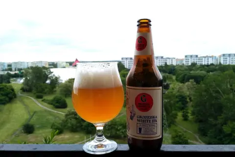Grodziska White IPA w szkle i butelce, z widokiem na zielone miasto. Idealne na letni wieczór.