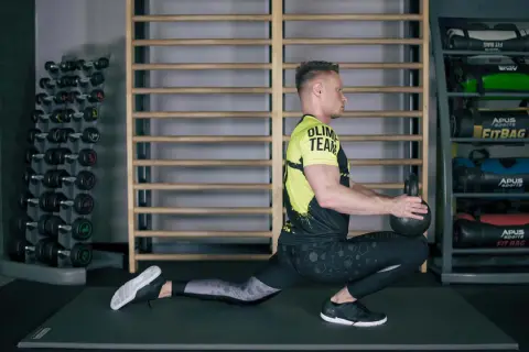 Ćwiczący wykonuje głęboki wykrok z kettlebell, co jest świetnym ćwiczeniem na mobilizację stawu skokowego.