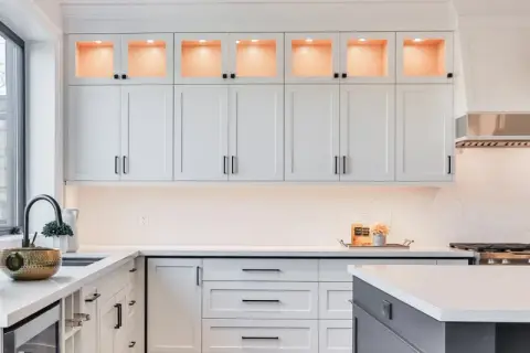 Elegante cocina moderna con gabinetes blancos, encimeras de cuarzo y detalles dorados. La iluminación cálida realza la decoración de cocinas.