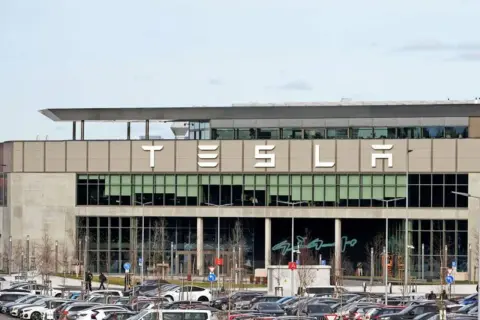 Tesla-Fabrik mit vielen Autos auf dem Parkplatz. Der Tesla-Betriebsrat vertritt die Interessen der Belegschaft.