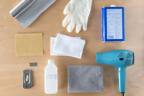 Kit pour savoir comment enlever du double face sur du carrelage : sèche-cheveux, grattoir, alcool isopropylique, gants, chiffons, papier de verre et rouleau d'aluminium.