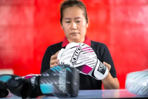 A woman inspects a pair of white YOKKAO sparring gloves. Other gloves, possibly bag gloves, are visible in the foreground.