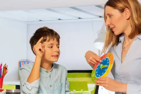 Bambino impara a leggere l'ora con una terapista occupazionale che usa un orologio colorato.