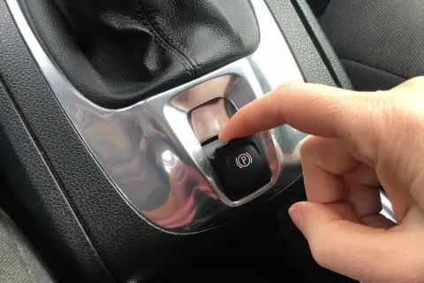Dito, un dito preme il pulsante del freno a mano elettronico, simbolo di sicurezza e modernità.