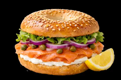 Un délicieux bagel saumon garni de fromage frais, oignons rouges, câpres et laitue, avec un quartier de citron à côté.