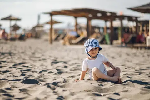 Uroczy maluch w kapelusiku na plaży. Idealne miejsce, gdzie na wakacje z rocznym dzieckiem.