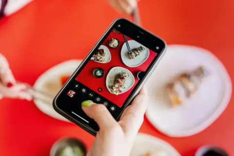 Une main ajuste le paramètre appareil photo Android pour photographier des sushis appétissants sur une table rouge vif.