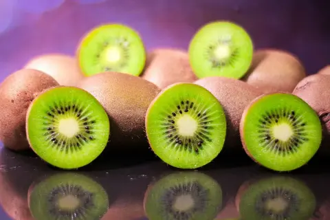 Kilka przekrojonych i całych kiwi na ciemnym tle z fioletowym rozmyciem w tle.