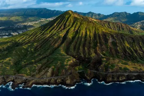 Widok z lotu ptaka na zielone wzgórza i ocean, gdzie leży Honolulu. W oddali widać zabudowania.