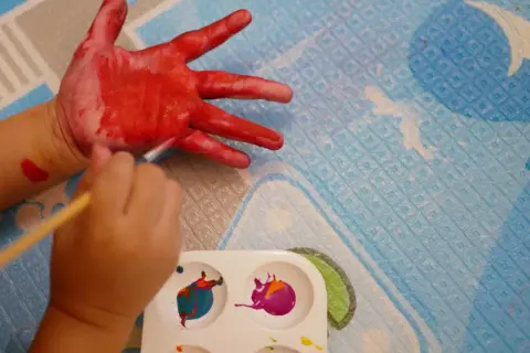 Dziecko maluje rękę na czerwono, przygotowując się do kreatywnego malowania farbami dla dzieci.