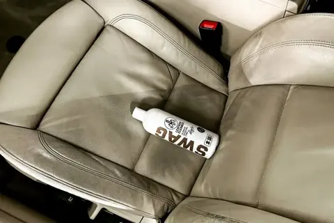 Butelka preparatu SWAG do czyszczenia skóry w aucie leży na jasnej, skórzanej kanapie. Idealny sposób, czym czyścić skórę w aucie.
