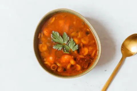 Herzhaftes Soljanka Rezept: Eine Schüssel voller würziger Suppe mit Oliven, Kapern und Kräutern, daneben ein goldener Löffel.