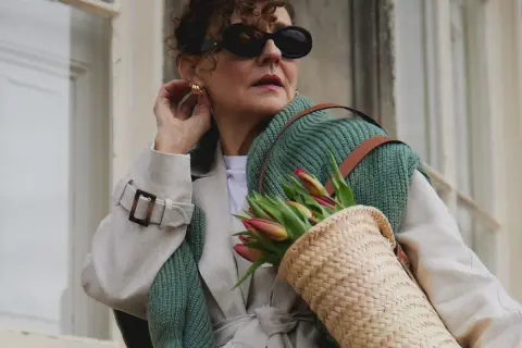Elegancka kobieta w okularach i płaszczu, z koszykiem pełnym tulipanów. Uosobienie stylu francuskiego w modzie damskiej.
