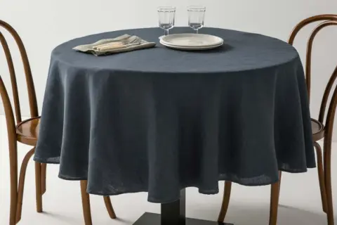 Table ronde avec nappe bleu nuit, deux chaises en bois et vaisselle. Une idée pour quel nappe choisir pour un dîner élégant.