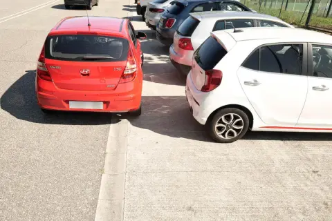 Coches aparcados en batería, un rojo y un blanco, junto a una acera.