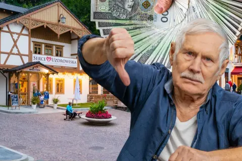 Starszy pan pokazuje kciuk w dół, trzymając stos banknotów. W tle budynek "Serce Uzdrowiska" w Szczawnicy.