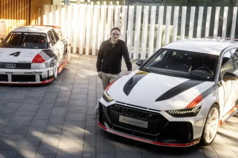 Mężczyzna stoi obok Audi RS6 Avant GT, z legendarnym Audi Quattro z lat 80. w tle.
