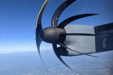 Wirujący śmigłowiec samolotu z efektem rolling shutter nad miastem i górami w oddali.