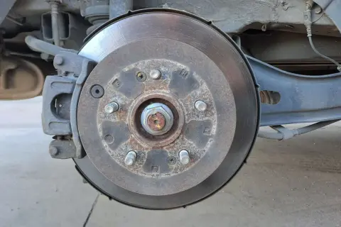 Gros plan sur un disque de frein usé, rouillé et marqué par l'usage. L'étrier de frein est visible, ainsi que des éléments de suspension.