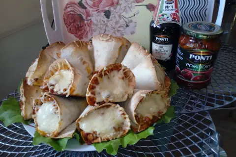 Pyszne rożki z tortilli z mięsem mielonym i ciągnącym się serem, podane na liściach sałaty. Obok butelka sosu balsamicznego i słoik pomidorów.
