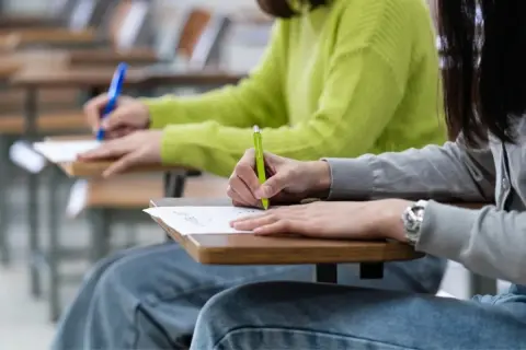 Uczniowie piszą egzamin CAE. Skupieni, z długopisami w dłoniach, wypełniają karty pracy.