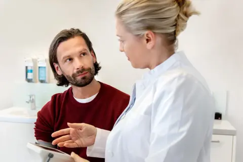 Ein sensibler Mann hört aufmerksam einer Ärztin zu, die ihm etwas auf einem Tablet erklärt.