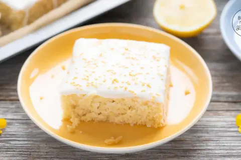Ein Stück saftiger, veganer Zitronenkuchen mit weißer Glasur und goldenen Streuseln auf einem gelben Teller.