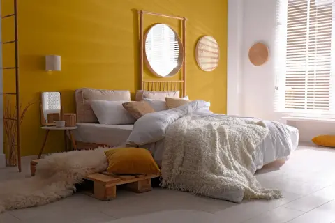 Une chambre d'adulte lumineuse avec un mur jaune vif, un lit douillet et une décoration murale en rotin.