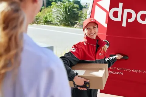 Kurierka DPD z uśmiechem przekazuje przesyłkę do doręczenia w punkcie pickup.
