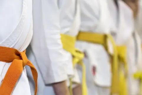 Zbliżenie na białe kimona z pomarańczowym i żółtym pasem, symbolizujące sztuki walki.