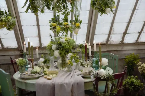 Vacker blomsterdekoration på bordet med ljus och grönska. En inbjudande dukning i ett växthus.