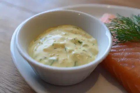 En skål med krämig gravlaxsås enkel, med dill och senapsfrön, bredvid en bit lax.