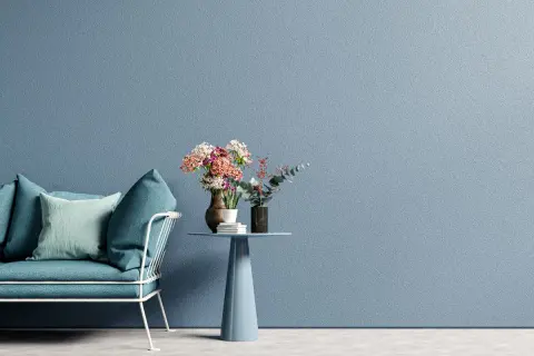 Divano blu e tavolino con fiori su muro azzurro, un esempio di moderni stili di pittura per interni.