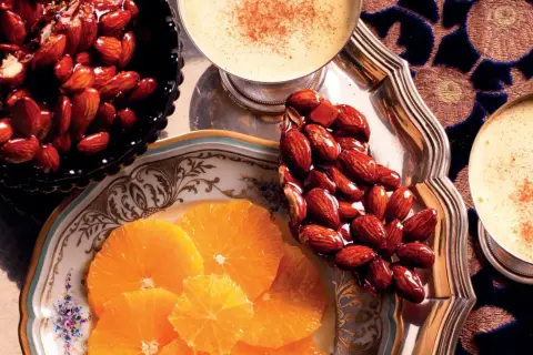 Un delizioso croccante di mandorle caramellate, accompagnato da fette d'arancia e bevande speziate.