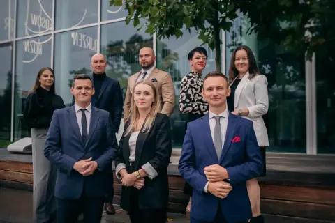 Grupa prawników w eleganckich strojach pozuje przed nowoczesnym budynkiem.