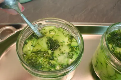Ein Glas Gurkensalat mit Dill wird mit einem Löffel vorbereitet, bereit zum Gurkensalat einkochen.
