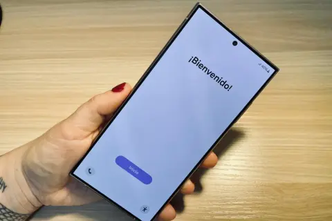 Mano sujetando un móvil listo para formatear. Pantalla de bienvenida con el botón "Inicio" visible.