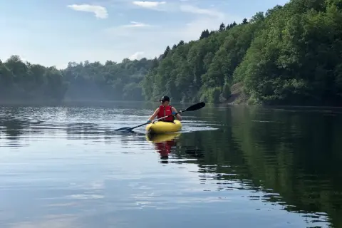 Person in gelbem Kajak genießt eine friedliche Kanu fahrt auf einem ruhigen See, umgeben von üppigen grünen Wäldern.