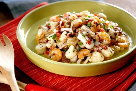 Deliciosa ensalada de marisco con camarones, calamares y vieiras, aderezada con hierbas frescas y pimientos.