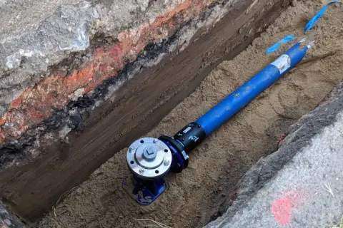 Blaues Rohr mit Ventil in einem ausgehobenen Graben.