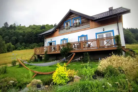 Dom z drewnianym tarasem i hamakiem w ogrodzie, otoczony zielenią. Idealne miejsce, by odpocząć i zastanowić się, gdzie w Bieszczady.