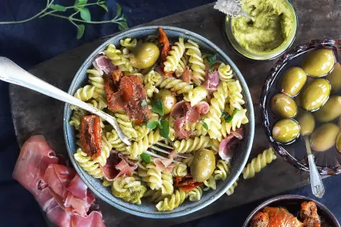 Pasta salad with pesto, sun-dried tomatoes, olives, and prosciutto.