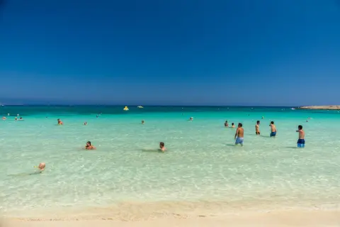 Ludzie kąpią się w krystalicznie czystej wodzie na plaży Makronissos. Słońce świeci, a niebo jest bezchmurne.